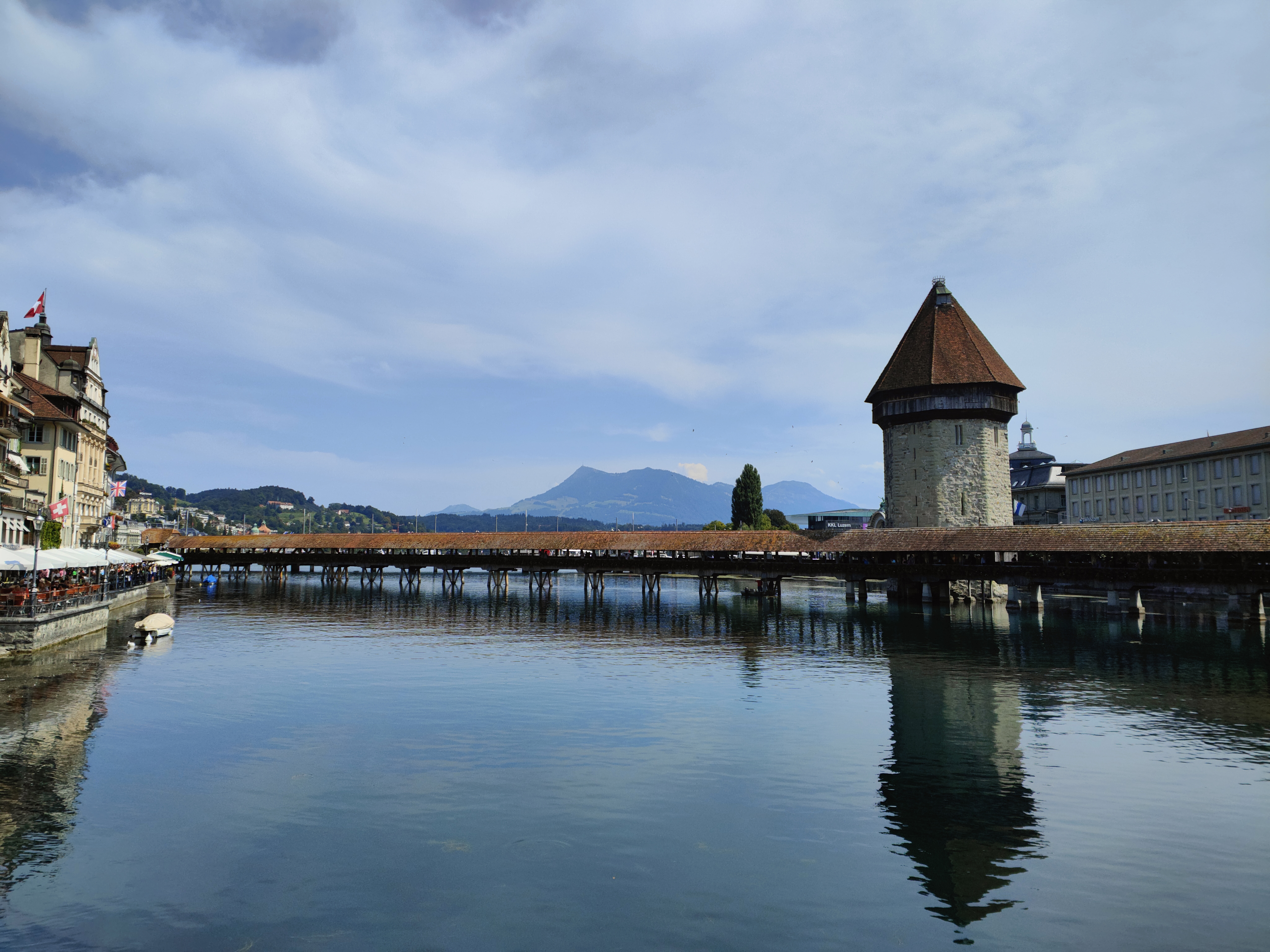 Le pont de la Chapelle franchit la Reuss à Lucerne ; sa tour d'eau octogonale en pierre, coiffée d'un toit conique, se reflète dans l'eau devant les façades des quais.
